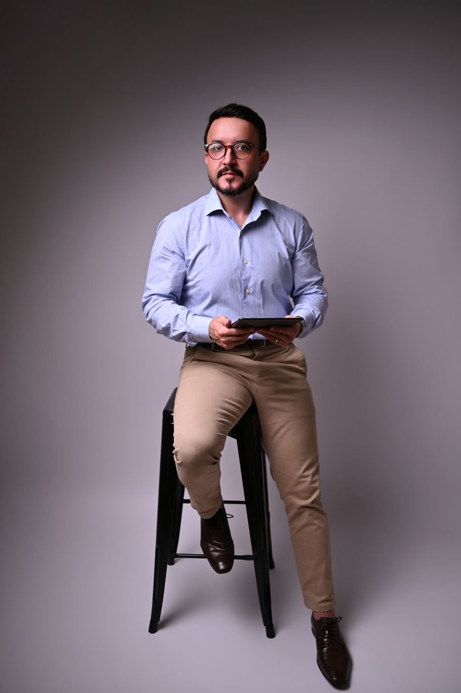 Dr. Fábio Baquero de camisa azul, sentado em uma banqueta segurando um iPad